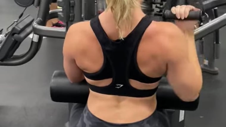 long-haired person in gym doing single-arm back exercise with cable