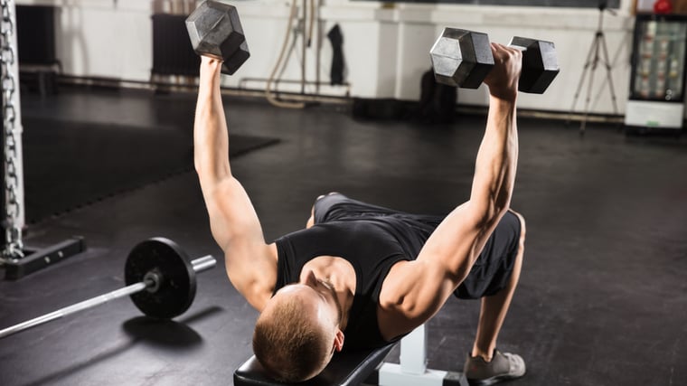 Man in gym on flat bench lifting dumbbells